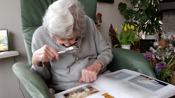 Oude vrouw die met loep een foto
bekijkt
