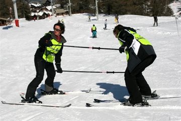 voorbeeld van begeleider en vb-skier die m.b.v. twee slalomstangen  met
elkaar verbonden zijn. De begeleider skiet achterwaarts en kijkt de vb-skier
in het gezicht.