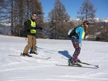 Voorbeeld van begeleider en vb-skier die met elkaar verbonden zijn d.m.v. een
tuigje. De begeleider skiet achtger de vb-skier
aan.