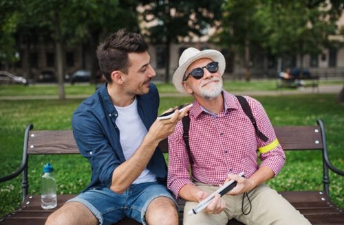 jonge man en blinde senior zittend op bench in park in de stad, voeren een
gesprek 