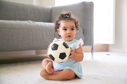 Peuter meisje zit op de grond met
voetbal