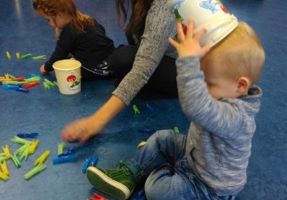 KInd dat met gekleurde wasknijpers en een emmertje speelt