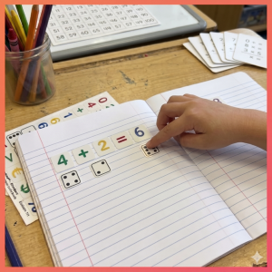 Een educatieve setting waarbij een kind leert rekenen met behulp van Stactiles
Cijfers set. In een gelinieerd schrift is de som 4 + 2 = 6 gevormd met
kleurrijke, voelbare cijferstickers. Onder de cijfers zijn bijbehorende tactiele
dobbelsteen-stickers geplakt om de hoeveelheden visueel en voelbaar te maken.
Een kinderhand voelt de sticker met zes stippen.