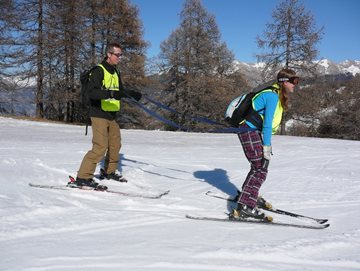 Voorbeeld van begeleider en vb-skier die met elkaar verbonden zijn d.m.v. een
tuigje. De begeleider skiet achtger de vb-skier
aan.