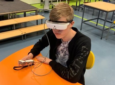 Leerling aan tafel met eSight bril op en controler in zijn
hand