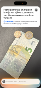 Foto van een bankbiljet en een paar euromunten, met daarbij de gedetailleerde beschrijving die Visuele Intelligentie genereert: “Hier ligt in totaal 6,05 euro: een briefje van 5 euro, een munt van één euro en een munt van 5 cent.” 