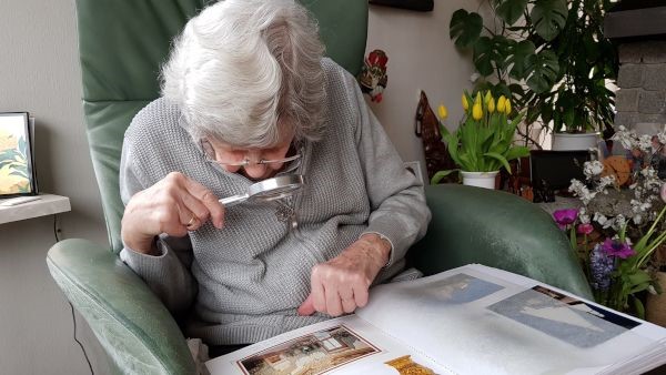 Oude vrouw die met loep een foto
bekijkt