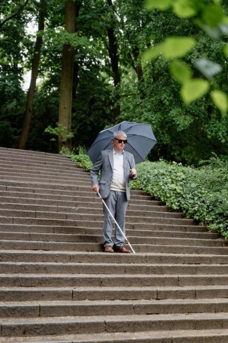 Blinde man daalt een lange trap af in het park met behulp van zijn
geleidestok