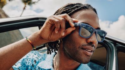 Man met de Meta Ray Ban bril op. Hij houdt zijn vinger op de knop houdt om een
foto of video te maken. 