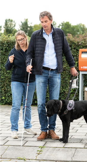 Man, vrouw en blindengeleidehond in een
trainingssituatie