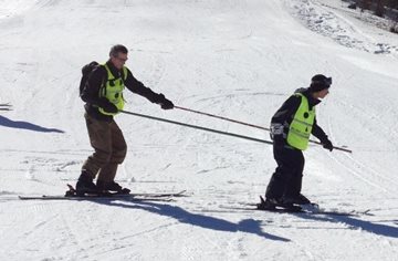 voorbeeld van begeleider en vb-skier die achter elkaar skieen en met twee
slalomstangen met elkaar verbonden zijn. De begeleider skiet achter de
vb-skier aan en kijkt de vb-skier in de
rug.