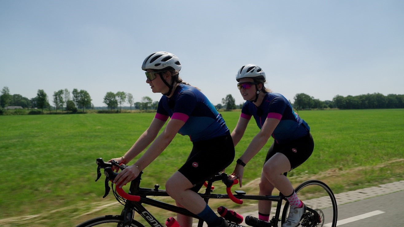 Wielrenster met visuele en auditieve beperking samen met haar begeleidster op
de wielrenfiets,  