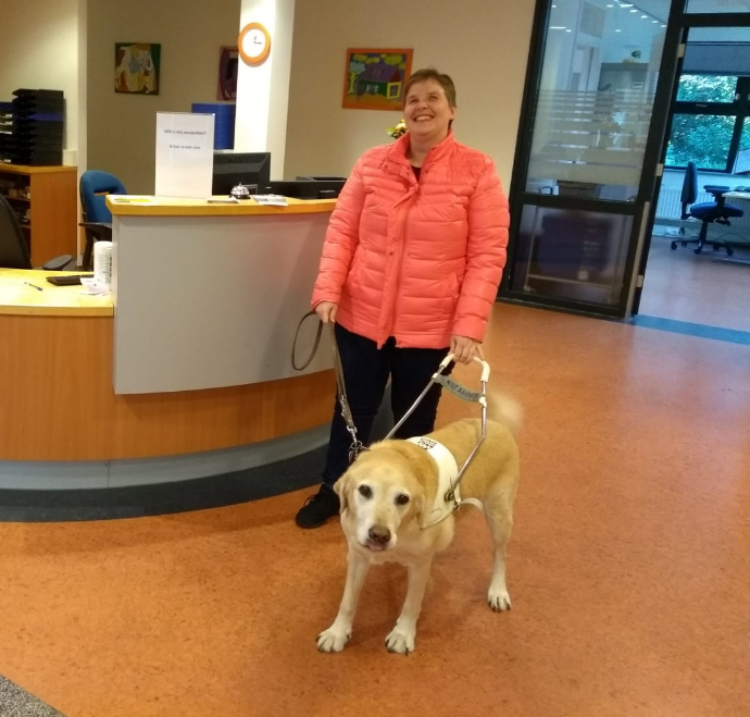 Carmen met geleidehond Nano in tuig voor de balie op haar
werk