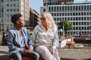 Twee vrouwen, waarvan een slechtziend, in gesprek op een bankje
buiten