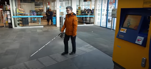 Vrouw met geleidestok loopt over geieidelijn op het
station